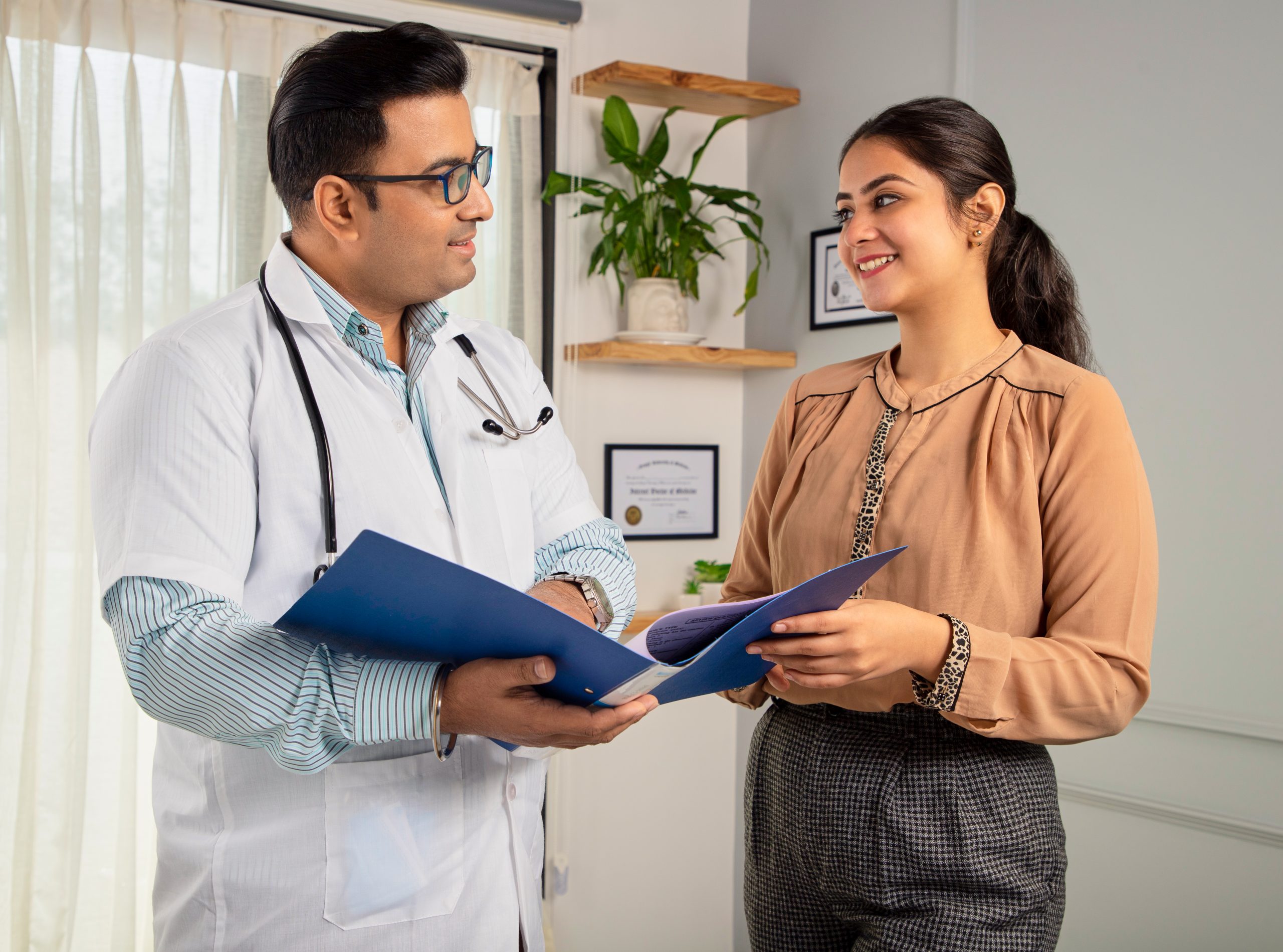 Asian Indian male physician holding report file in hand and giving consultation to a smiling female.